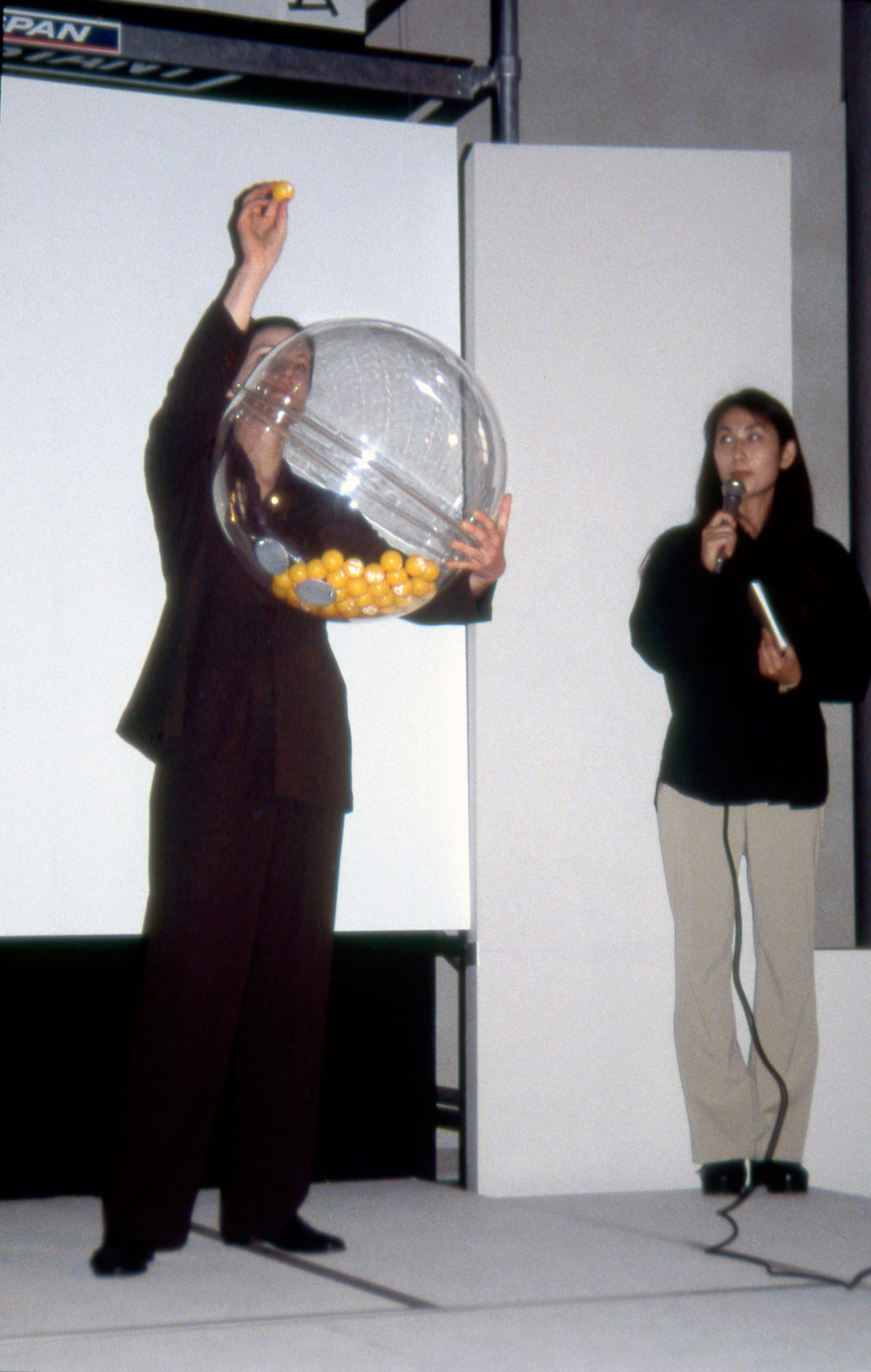 Art, artwork. A performance entitled "Nika's Game of Chance" by Nika Span / Nika Špan. Material: 49 numbered table tennis balls, a Plexiglas sphere, a fan, 20 copies of a lottery ticket, a female assistant. Exhibition: Academy Exchange, School of Art and Design, Seoul, Korea; Tokyo Geijutsu, Tokyo, Japan.